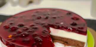 Μία τούρτα από πολύστρωτο cheese κέικ με βάση σοκολατένιου παντεσπανι λευκή κρεμώδη μους τυριού και κόκκινη στρώση ζελέ με ολόκληρα κεράσια.