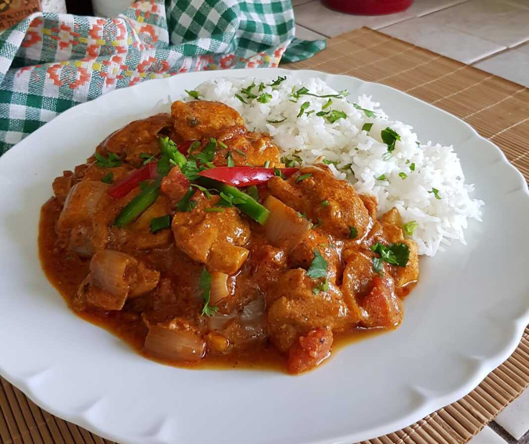 Ένα πιάτα με κοτόπουλο τίκα μασάλα, που περιέχει κομμάτια κοτόπουλου σε μια πλούσια πορτοκαλί-κόκκινη σάλτσα, με αρωματικό ρύζι Basmati δίπλα.