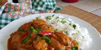 Ένα πιάτα με κοτόπουλο τίκα μασάλα, που περιέχει κομμάτια κοτόπουλου σε μια πλούσια πορτοκαλί-κόκκινη σάλτσα, με αρωματικό ρύζι Basmati δίπλα.