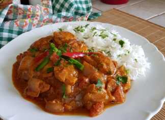 Ένα πιάτα με κοτόπουλο τίκα μασάλα, που περιέχει κομμάτια κοτόπουλου σε μια πλούσια πορτοκαλί-κόκκινη σάλτσα, με αρωματικό ρύζι Basmati δίπλα.