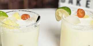 Δύο ποτήρια με δροσερό αναψυκτικό με ανανά και καρύδα, γεμάτο παγάκια, κομμάτια ανανά, και διακοσμημένο με ένα κεράσι και τριμμένη καρύδα στο χείλος.