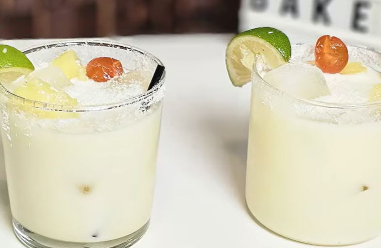 drosero poto anana karida Δύο ποτήρια με δροσερό αναψυκτικό με ανανά και καρύδα, γεμάτο παγάκια, κομμάτια ανανά, και διακοσμημένο με ένα κεράσι και τριμμένη καρύδα στο χείλος.