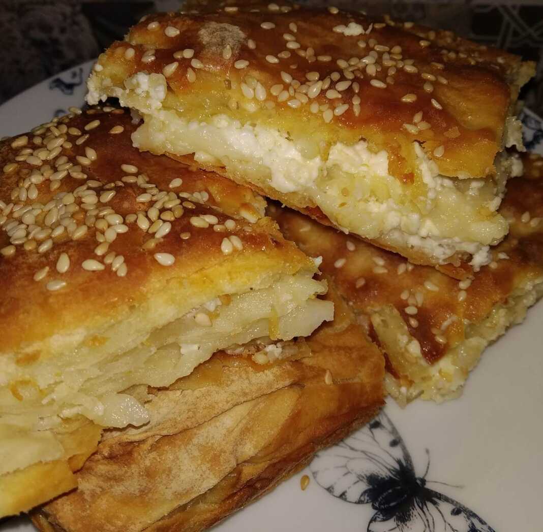 Μια φρεσκοψημένη, χρυσαφένια τυρόπιτα, κομμένη σε τετράγωνα κομμάτια, με το φύλλο της να φαίνεται τραγανό και αφράτο.