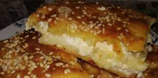 Μια φρεσκοψημένη, χρυσαφένια τυρόπιτα, κομμένη σε τετράγωνα κομμάτια, με το φύλλο της να φαίνεται τραγανό και αφράτο.