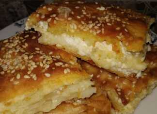 Μια φρεσκοψημένη, χρυσαφένια τυρόπιτα, κομμένη σε τετράγωνα κομμάτια, με το φύλλο της να φαίνεται τραγανό και αφράτο.