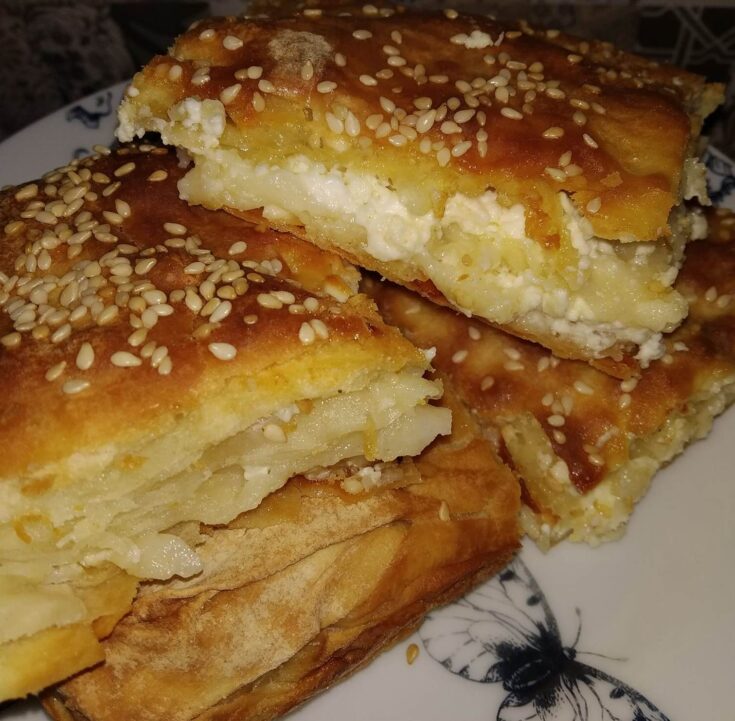 Μια φρεσκοψημένη, χρυσαφένια τυρόπιτα, κομμένη σε τετράγωνα κομμάτια, με το φύλλο της να φαίνεται τραγανό και αφράτο.