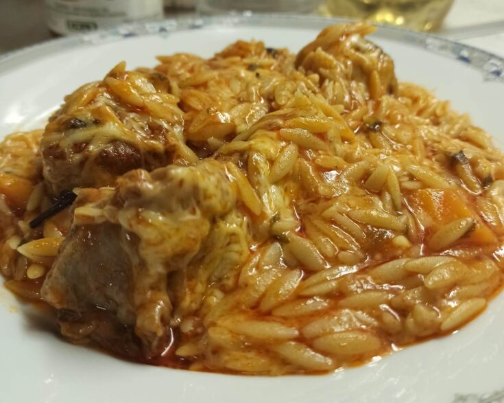 Μια γάστρα γεμάτη με ζεστό γιουβέτσι μοσχαράκι, με κόκκινη σάλτσα, κριθαράκι και λιωμένο τριμμένο τυρί στην επιφάνεια.