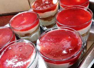 7 γυάλινα μπολακια με στρώσεις από τριμμένα μπισκότα, λευκή κρέμα γιαουρτιού και κόκκινη μαρμελάδα φράουλα στην κορυφή.