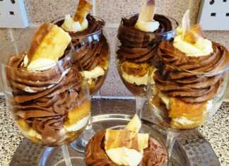 Πέντε γυάλινα ποτήρια με στρώσεις από βρεγμένα μπισκότα, άσπρη σαντιγί και σοκολατένια σαντιγί, στολισμένα με ροζ λουλούδια ζαχαρόπαστας.