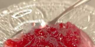 Ένα πιατακι γεμάτο με κόκκινο-ροζ γλυκό του κουταλιού τριαντάφυλλο, με ολόκληρα πέταλα ορατά μέσα στο σιρόπι.