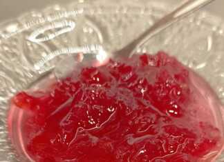 Ένα πιατακι γεμάτο με κόκκινο-ροζ γλυκό του κουταλιού τριαντάφυλλο, με ολόκληρα πέταλα ορατά μέσα στο σιρόπι.