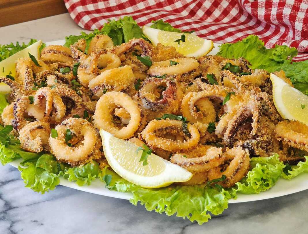 Ένα πιάτο γεμάτο με χρυσαφένια, τραγανά Καλαμαράκια στο φούρνο, γαρνιρισμένα με φέτες λεμονιού και φρέσκο μαϊντανό.