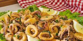 Ένα πιάτο γεμάτο με χρυσαφένια, τραγανά Καλαμαράκια στο φούρνο, γαρνιρισμένα με φέτες λεμονιού και φρέσκο μαϊντανό.