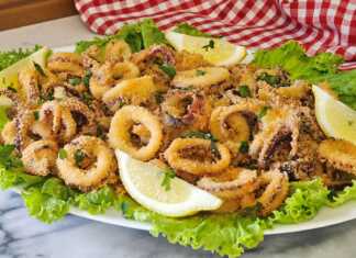 Ένα πιάτο γεμάτο με χρυσαφένια, τραγανά Καλαμαράκια στο φούρνο, γαρνιρισμένα με φέτες λεμονιού και φρέσκο μαϊντανό.