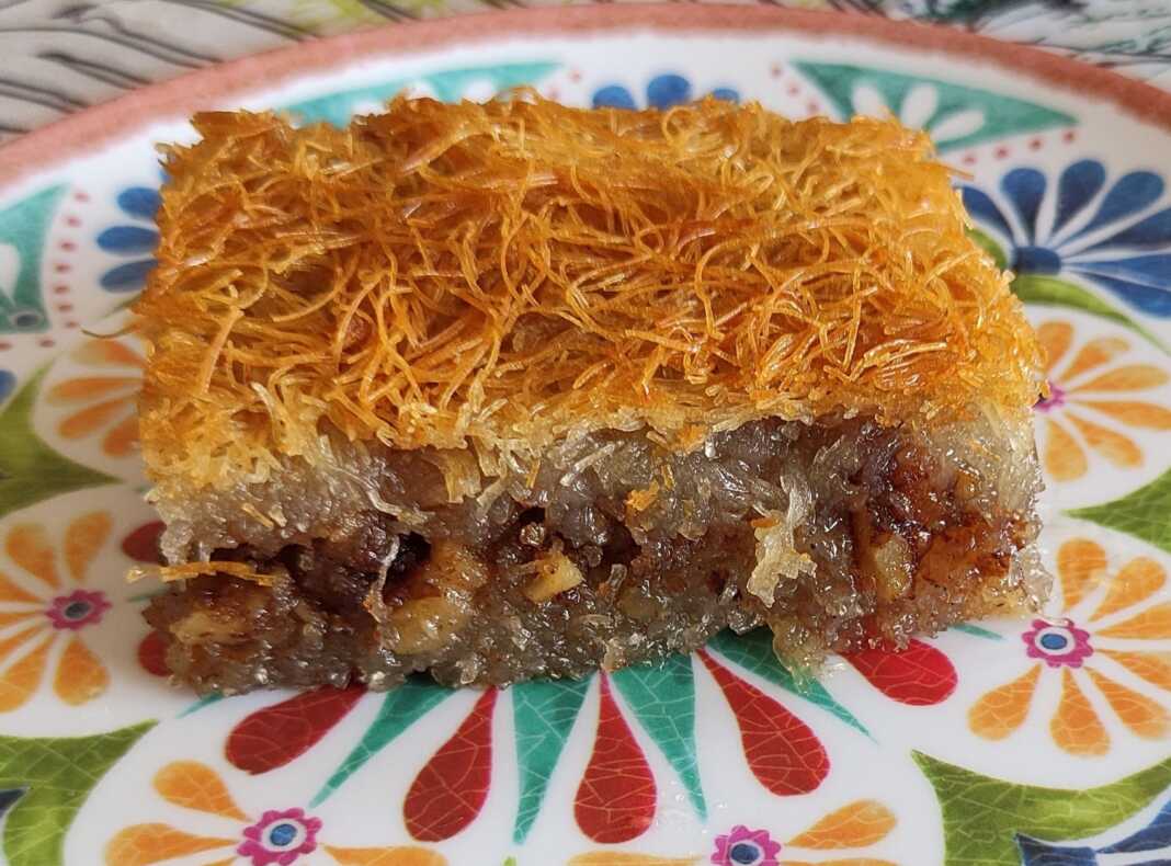 Ένα κομμάτι χρυσαφένιο, σιροπιασμένο κανταΐφι, πασπαλισμένο με τριμμένο καρύδι και κανέλα.