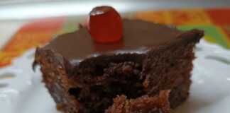 Ένα τετράγωνο κομμάτι από λαχταριστή, σιροπιασμένη καρυδόπιτα με καρύδια, καλυμμένη με ένα γυαλιστερό, σκούρο σοκολατένιο γλάσο.