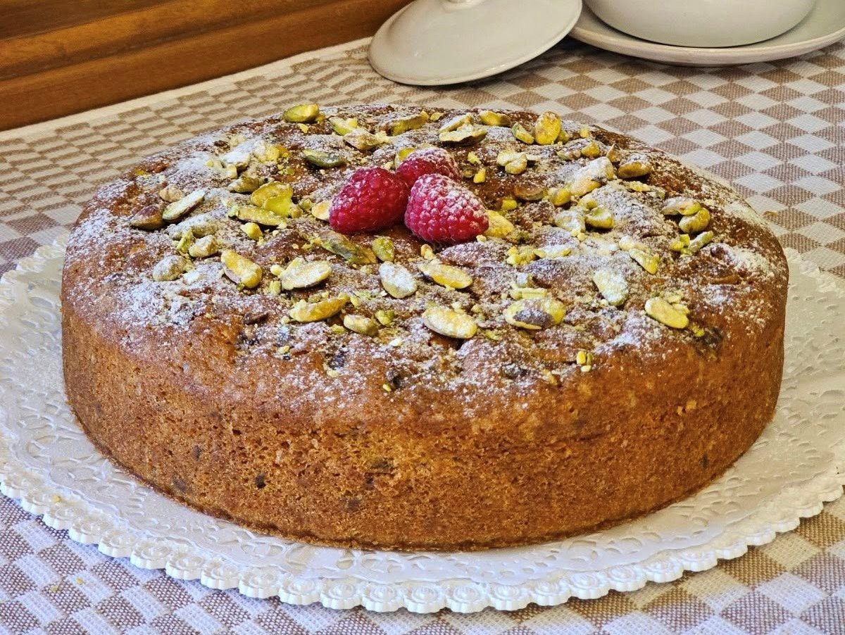 Ένα πλούσιο κέικ με επικάλυψη crumble και φιστίκια, τοποθετημένο σε ένα πιάτο.