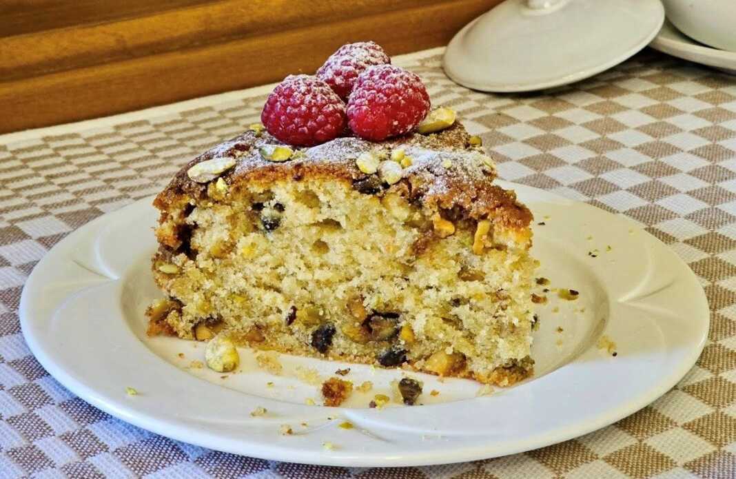 Ένα κομμάτι από ένα πλούσιο κέικ με επικάλυψη crumble και φιστίκια, τοποθετημένο σε ένα πιάτο.