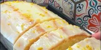 Αφράτο, κίτρινο κέικ λεμονιού, καλυμμένο με γλάσο λεμονιού και πασπαλισμένη με ξύσμα, με φόντο το υπόλοιπο κέικ.