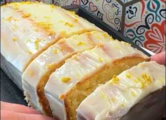 Αφράτο, κίτρινο κέικ λεμονιού, καλυμμένο με γλάσο λεμονιού και πασπαλισμένη με ξύσμα, με φόντο το υπόλοιπο κέικ.