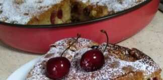 Ένα κομμάτι από αφράτο κέικ με κεράσια, πασπαλισμένο με άχνη ζάχαρη. Τα κεράσια είναι ορατά μέσα στο κέικ.