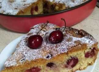 Ένα κομμάτι από αφράτο κέικ με κεράσια, πασπαλισμένο με άχνη ζάχαρη. Τα κεράσια είναι ορατά μέσα στο κέικ.