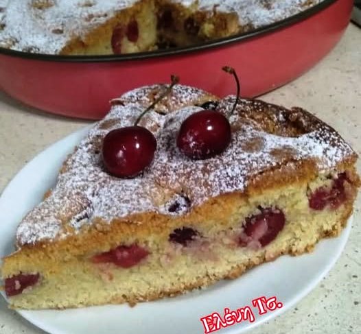 keik me kerasia Ένα κομμάτι από αφράτο κέικ με κεράσια, πασπαλισμένο με άχνη ζάχαρη. Τα κεράσια είναι ορατά μέσα στο κέικ.