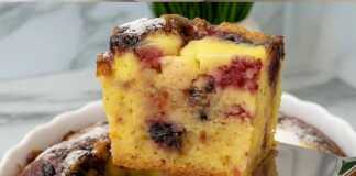 Ενα χρυσαφένιο κέικ με κεράσια και κρεμώδη γέμιση, πασπαλισμένη με ζάχαρη άχνη, σερβιρισμένη σε μια λευκή πιατέλα.