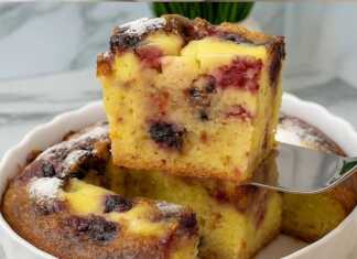 Ενα χρυσαφένιο κέικ με κεράσια και κρεμώδη γέμιση, πασπαλισμένη με ζάχαρη άχνη, σερβιρισμένη σε μια λευκή πιατέλα.