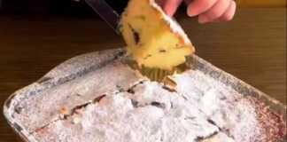 Ένα κομμάτι από ένα αφράτο, χρυσαφένιο κέικ πασπαλισμένο με άχνη ζάχαρη, με κομμάτια σοκολάτας ορατά μέσα στη ζύμη.