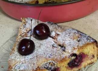 Μια φρεσκοψημένη, χρυσαφένια κερασόπιτα με πολλά κόκκινα κεράσια στην επιφάνεια, πασπαλισμένη με ζάχαρη άχνη, κομμένη σε κομμάτια.