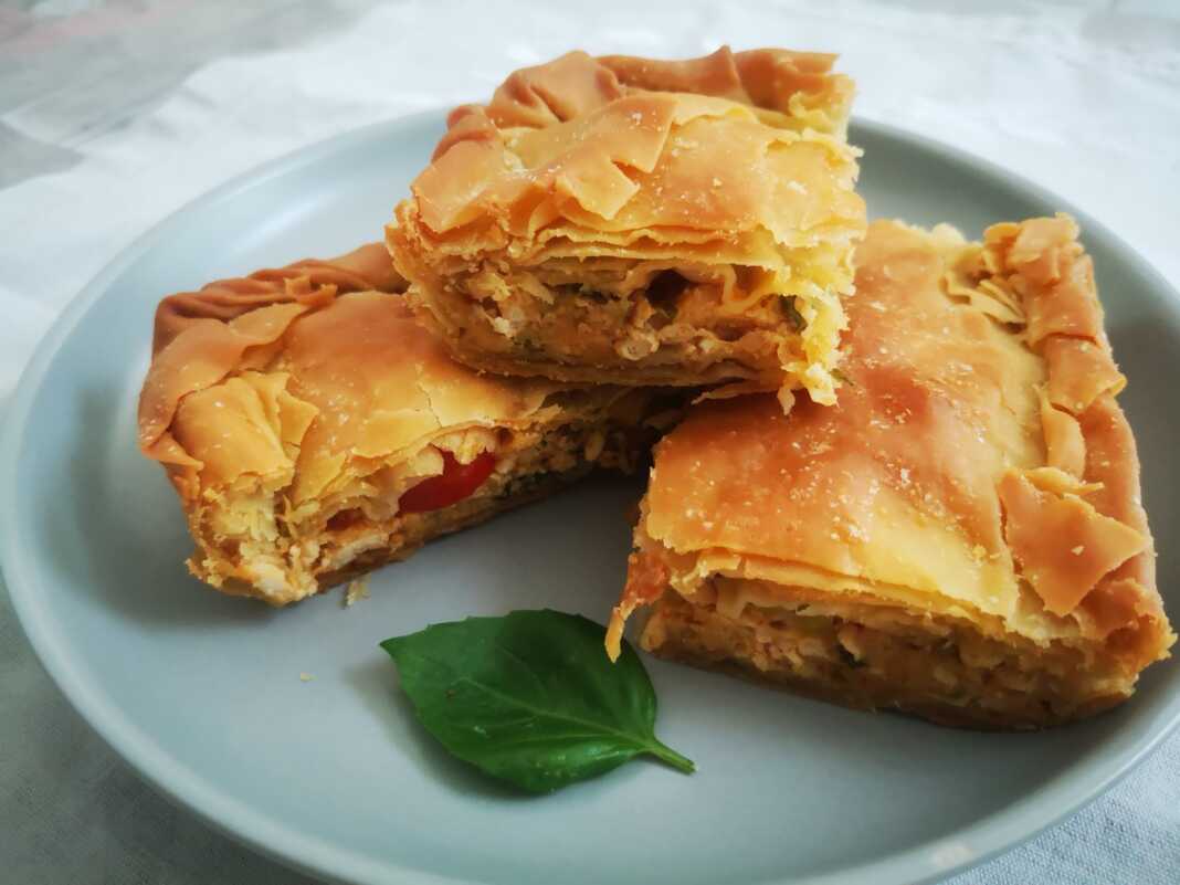 Μια φρεσκοψημένη, χρυσαφένια κιμαδόπιτα κοτόπουλου, κομμένη σε τετράγωνα κομμάτια, που αναδεικνύει τις στρώσεις του τραγανού φύλλου.