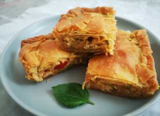 Μια φρεσκοψημένη, χρυσαφένια κιμαδόπιτα κοτόπουλου, κομμένη σε τετράγωνα κομμάτια, που αναδεικνύει τις στρώσεις του τραγανού φύλλου.