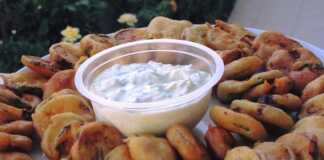 Ένα πιάτο με χρυσαφένιες τηγανιτές φέτες κολοκυθιού και μελιτζάνας δίπλα σε ένα μπολάκι με λευκό τζατζίκι.