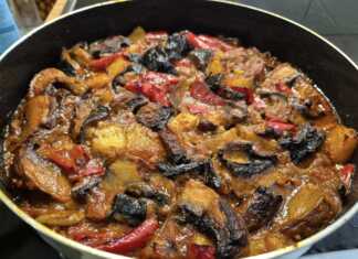 Ένα ταψί με λαχταριστά ψητά λαχανικά, όπως μελιτζάνες, πιπεριές και πατάτες, μέσα σε κόκκινη σάλτσα, με φρέσκα βότανα από πάνω.