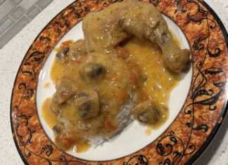 Ένα πιάτο με κοτόπουλο λεμονάτο, με πλούσια κίτρινη σάλτσα, κομμάτια μανιταριών και ρύζι μπασμάτι στο πλάι.