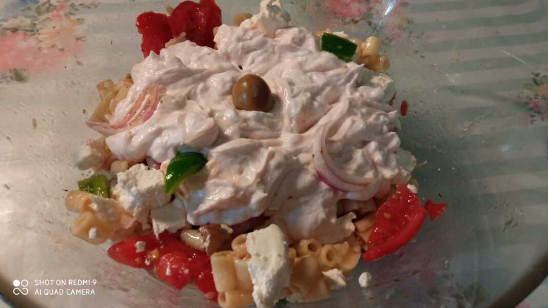 Ένα μεγάλο μπολ γεμάτο με πολύχρωμη χωριάτικη μακαρονοσαλάτα, με κοντά ζυμαρικά, κομμένες ντομάτες, πιπεριές, ελιές και θρυμματισμένη φέτα.