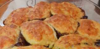 Ένα ταψί με γεμιστές μελιτζάνες σε σχήμα βαρκούλας, καλυμμένες με λευκή μπεσαμέλ και λίγο τριμμένο τυρί, ψημένες μέχρι να ροδίσουν.