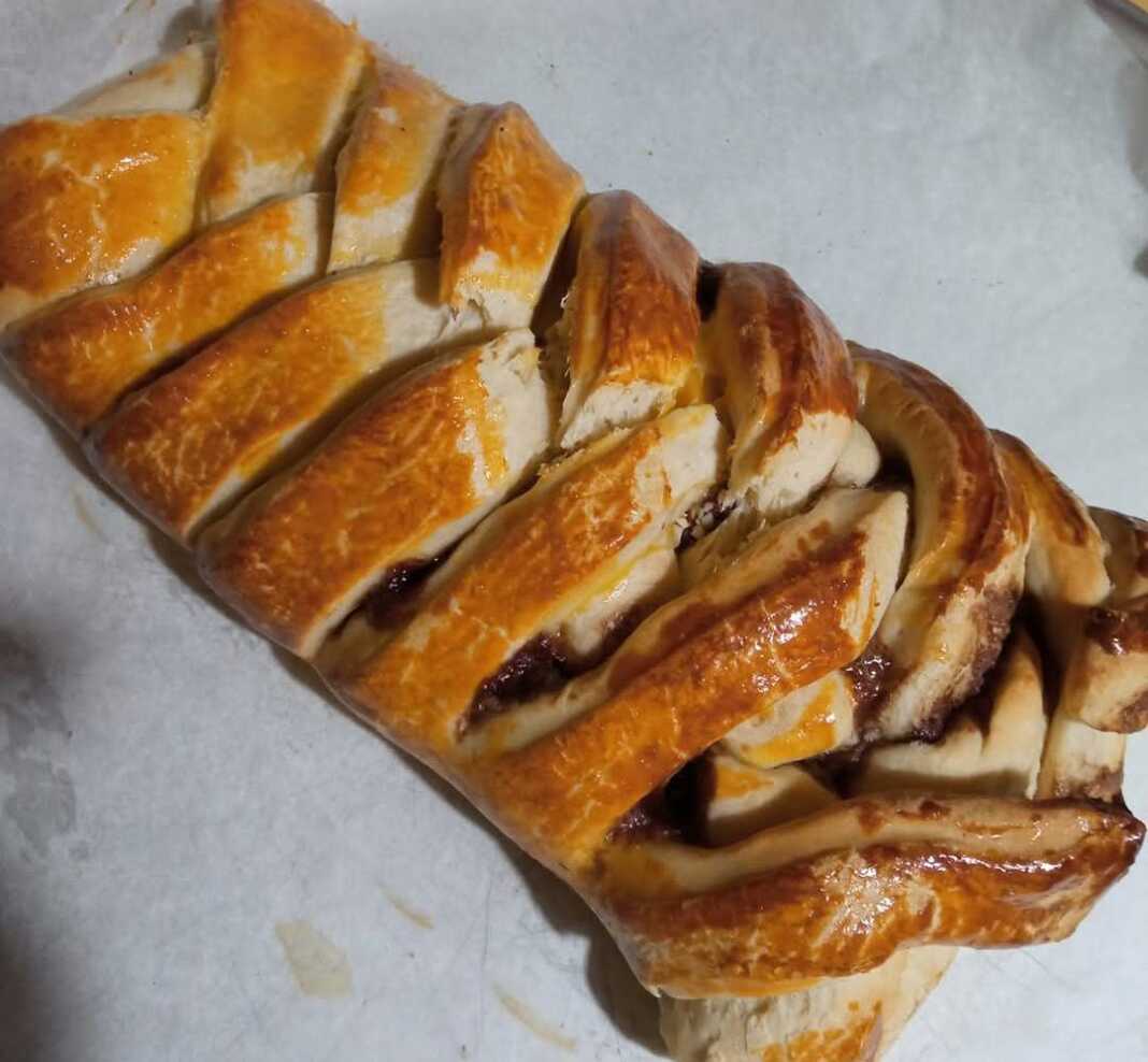 merentolixoudia Ένα οβάλ γλυκό ψωμί με γέμιση πραλίνας και ξηρών καρπών, διακοσμημένο με περίτεχνο σχέδιο από στριμμένες λωρίδες ζύμης.