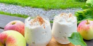 Ένα ποτήρι γεμάτο με αφράτο, ανοιχτόχρωμο επιδόρπιο μήλου, πασπαλισμένο με κανέλα, έτοιμο για σερβίρισμα.