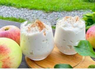 Ένα ποτήρι γεμάτο με αφράτο, ανοιχτόχρωμο επιδόρπιο μήλου, πασπαλισμένο με κανέλα, έτοιμο για σερβίρισμα.