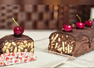 Ένα κομμένο κομμάτι από καλοκαιρινό μωσαϊκό με εμφανή κομμάτια μπισκότου, κερασιών και ξηρών καρπών, καλυμμένο με σοκολάτα, σερβιρισμένο σε λευκό πιάτο.