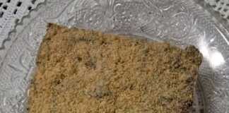 Ένα κομμάτι μωσαϊκό (κορμός σοκολάτας) με εμφανή κομματάκια μπισκότου, πασπαλισμένο με τριμμένο μπισκότο.