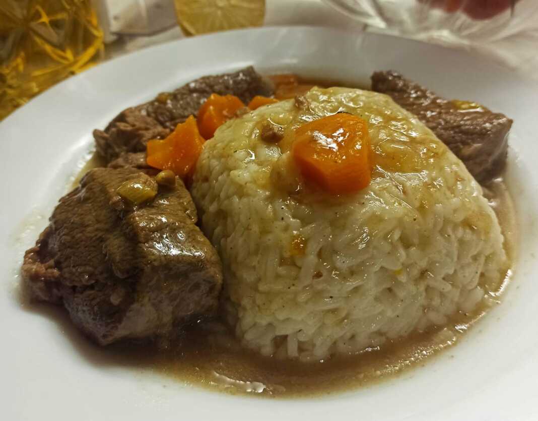 mosxari rizi Ένα πιάτο με μαγειρεμένο μοσχάρι σε κομμάτια, περιχυμένο με μια πηχτή, καστανή σάλτσα, δίπλα σε ένα πιάτο με αφράτο πιλάφι.