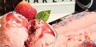 Ένα μπολ γεμάτο αφράτο, ροζ παγωτό φράουλα, διακοσμημένο με φρέσκες φράουλες και σιρόπι, έτοιμο για σερβίρισμα.