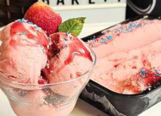 Ένα μπολ γεμάτο αφράτο, ροζ παγωτό φράουλα, διακοσμημένο με φρέσκες φράουλες και σιρόπι, έτοιμο για σερβίρισμα.