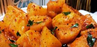 Ένα πιάτο με ζεστές πατάτες γιαχνί, περιχυμένες με κόκκινη σάλτσα, πασπαλισμένες με μαϊντανό και μπούκοβο, με ένα κομμάτι φέτας στο πλάι.