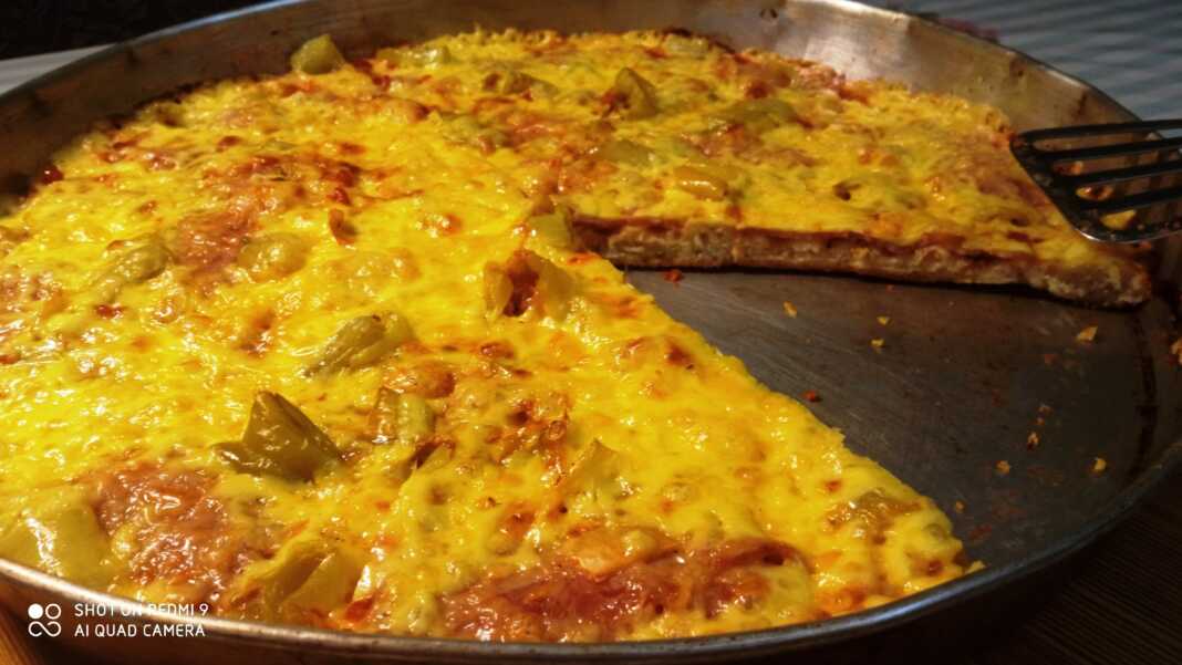 Μια φρεσκοψημένη, λαχταριστή πίτσα με χρυσαφένια κρούστα, λιωμένο τυρί, μπέικον και πιπεριές, πάνω σε ένα ταψί.