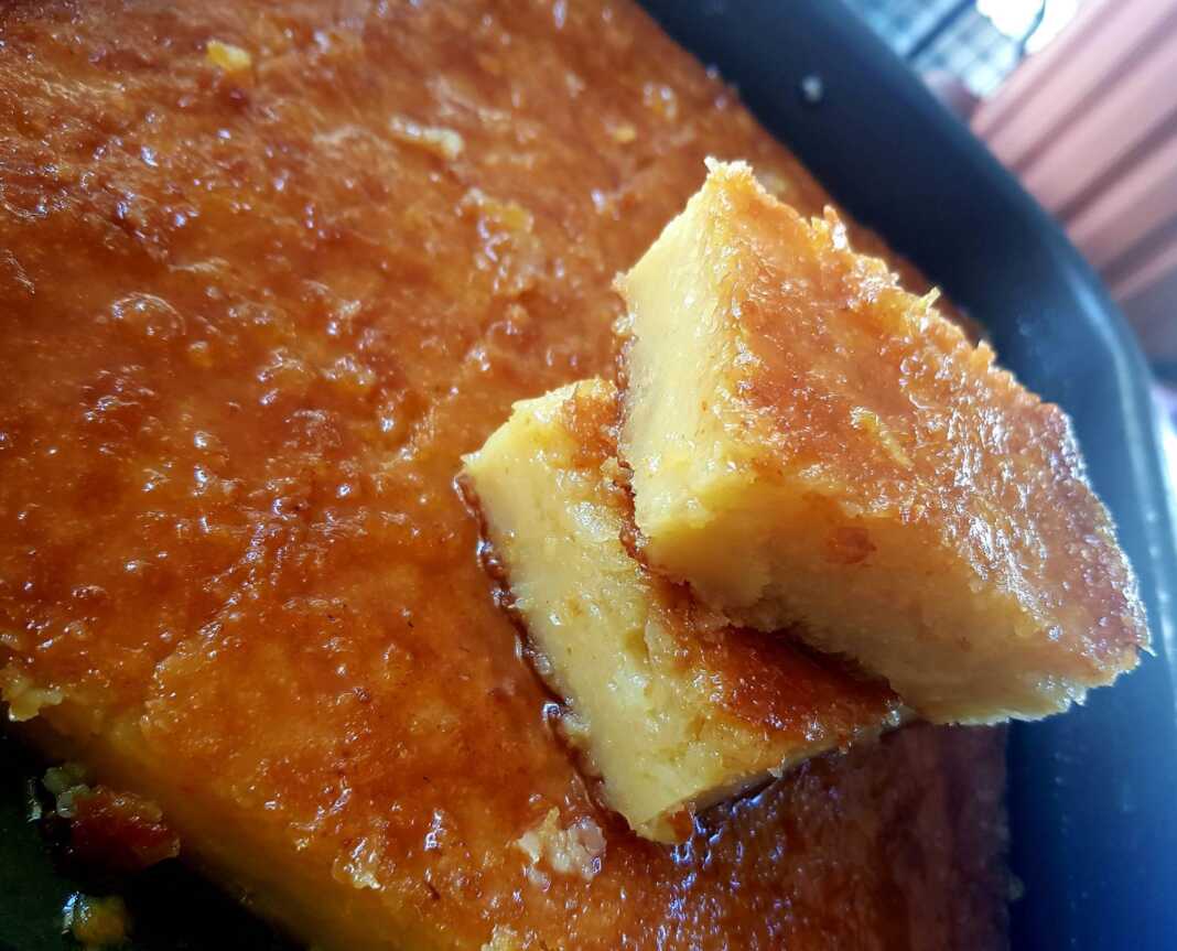 Ένα ταψί πορτοκαλόπιτας, που δείχνει την πορώδη υφή του γλυκού και το χρυσαφένιο του χρώμα, περιχυμένο με σιρόπι.