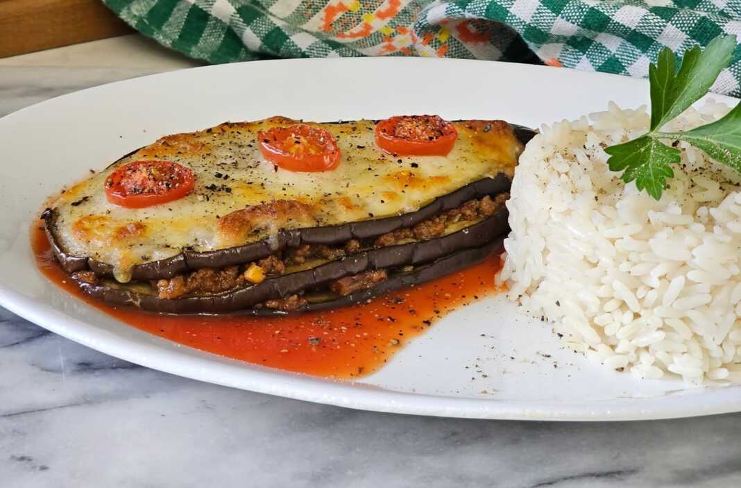 psites melitzanes me mosxari Ένα πιατο με ψητές μελιτζάνες γεμισμένες με κιμά και καλυμμένες με λιωμένη μοτσαρέλα και ντοματίνια, έτοιμες για σερβίρισμα.